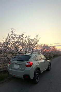 the car is parked on the side of the road in front of blossoming trees