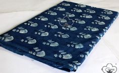 a blue blanket with leaves on it laying on a white bed sheet that is folded up