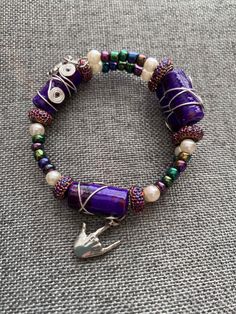 a purple beaded bracelet with an owl charm and charms on the clasp is sitting on a gray surface