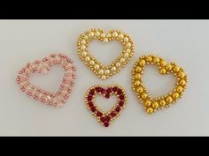 three beaded heart shaped brooches on a white surface, one in gold, the other in red