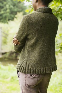 a woman wearing a green sweater standing in front of a tree with her back to the camera