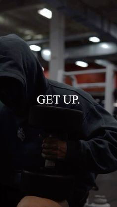 a man wearing a hoodie and holding a weight scale with the words get up written on it