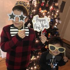 two young boys standing next to each other in front of a christmas tree with decorations