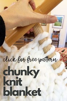 a hand is holding a wooden knitting needle over a pile of white knitted wool