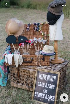 a wicker picnic basket with hats, sunglasses and props on display in the grass next to a sign that says selte booth grab a prop and strike a pose