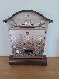 a small wooden box with birds painted on the side and flowers in the middle, sitting on a table