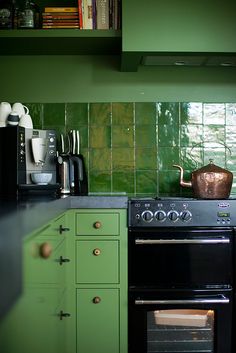 a stove top oven sitting inside of a kitchen next to green cabinets and counter tops