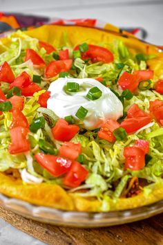 a salad with tomatoes, lettuce and sour cream on top in a pie pan