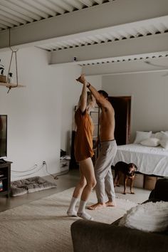 a man and woman are dancing in the living room while their dog watches from the couch