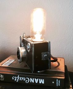 an old fashioned camera sitting on top of two books with a light bulb in the middle