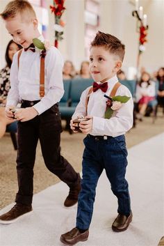 two young boys wearing suspenders and bow ties walk down the aisle at a wedding