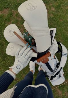 a person holding golf clubs in their hands on the grass with gloves and balls attached to them