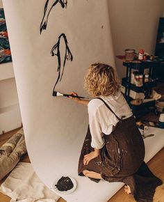 a woman is sitting on the floor and painting with black paint in front of a surfboard