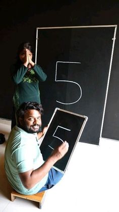 two people sitting on the floor in front of a blackboard with letters drawn on it