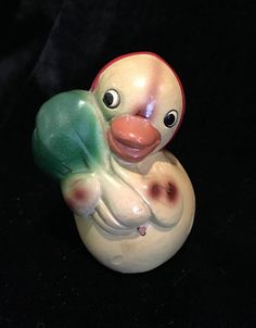 a small ceramic duck with green wings on it's head and beak, sitting on a black surface