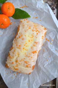 an orange cake sitting on top of a piece of paper next to two oranges