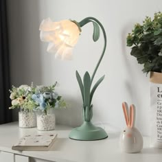 a white table topped with a green lamp next to a vase filled with flowers and plants