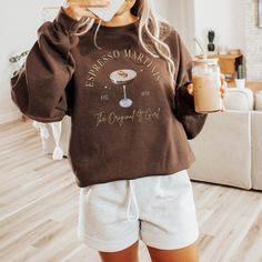 a woman holding a drink and wearing a brown sweatshirt with the words, coffee manias on it