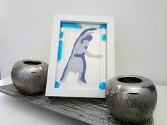 two silver vases sitting next to each other on a metal shelf in front of a picture frame