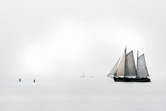 a sailboat sailing in the ocean on a foggy day with another boat nearby