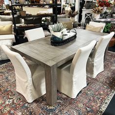 a dining room table with white chairs and rugs in front of the couches