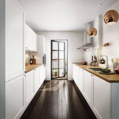 a kitchen with wooden floors and white cabinets, an open door leading to a balcony