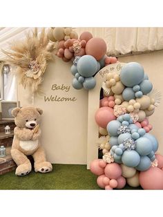 a teddy bear sitting in front of a welcome sign with balloons attached to the letters