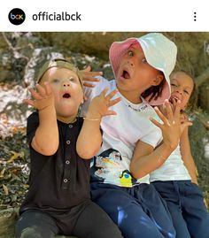 three young children sitting on the ground with their hands in the air and one holding his mouth open