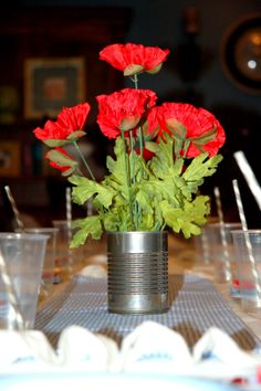 red carnations in a tin can on a table with empty cups and forks