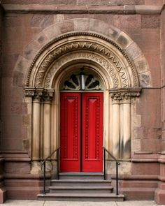 a red door is on the side of an old stone building with steps leading up to it