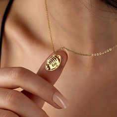 a woman's hand holding a gold necklace with a football charm on it