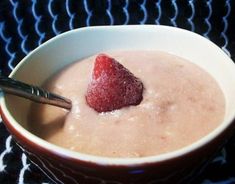 a bowl of oatmeal with a strawberry on top and spoon in it