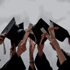 a group of people in graduation caps and gowns holding their hands up to the sky