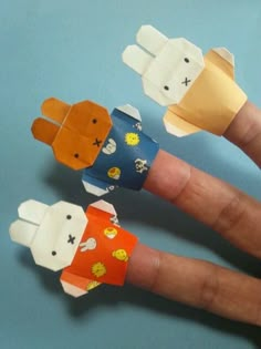 three hand made paper animals sitting on top of each other's fingers, with one being held up to the camera