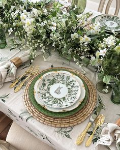 the table is set with plates, silverware and green floral centerpieces on it