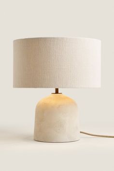 a white table lamp with a beige shade on the base and a cord attached to it