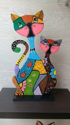 two colorful cats sitting on top of a shelf