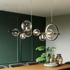 a dining room table and chairs with lights hanging from the ceiling above it, in front of green walls