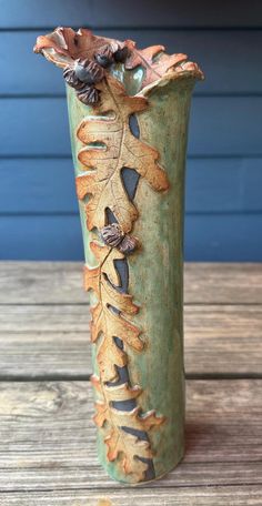 a green vase with leaves on it sitting on a wooden table