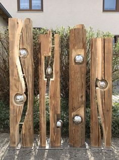 a sculpture made out of wood with metal knobs on it's sides in front of a house