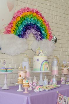 a table topped with lots of cake and cupcakes next to a white brick wall