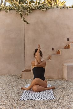 a woman in a black swimsuit sitting on a yoga mat with her hands up