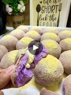 a person is holding a purple and yellow doughnut in front of some other pastries