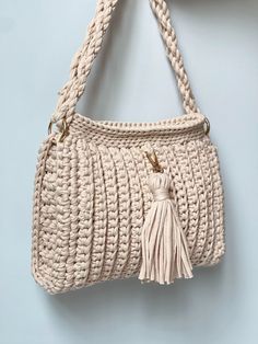 a crocheted bag hanging on the wall with a tasselled handle and fringe