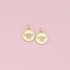 two small gold bee charms on a pink background with the word love written in it