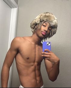 a shirtless man taking a selfie with his cell phone and wearing a furry hat