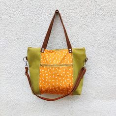 an orange and green handbag hanging on a white wall next to a brown leather strap