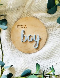 it's a boy wooden sign with eucalyptus leaves around it on a white blanket