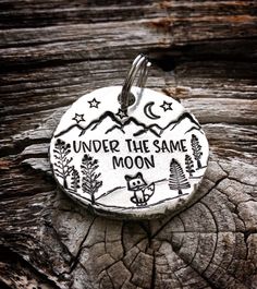 a metal charm with the words under the same moon on it sitting on top of a piece of wood