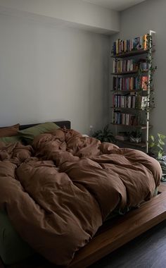 an unmade bed in a room with bookshelves and plants on the wall